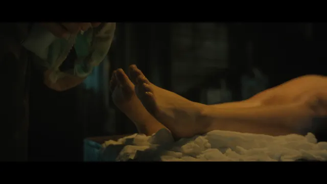 Addison Rae resting bare feet in a dimly lit screen scene.