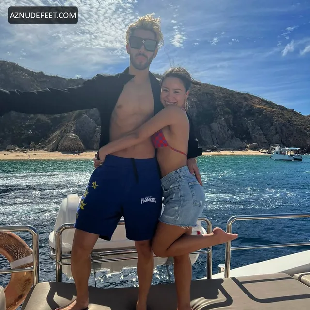 Cierra Ramirez in a casual crop top, jeans and sneakers beside her partner at the seaside.