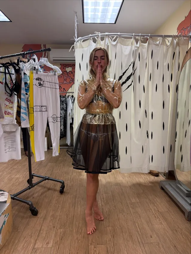 Addison Rae standing barefoot in a dressing room beside a clothing rack.