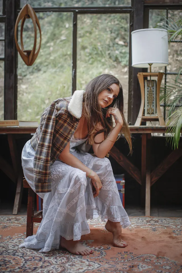 Lana Del Rey standing barefoot beside a piano in a layered skirt.