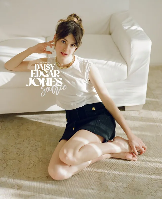 Daisy Edgar-Jones seated on a rug beside a white sofa.