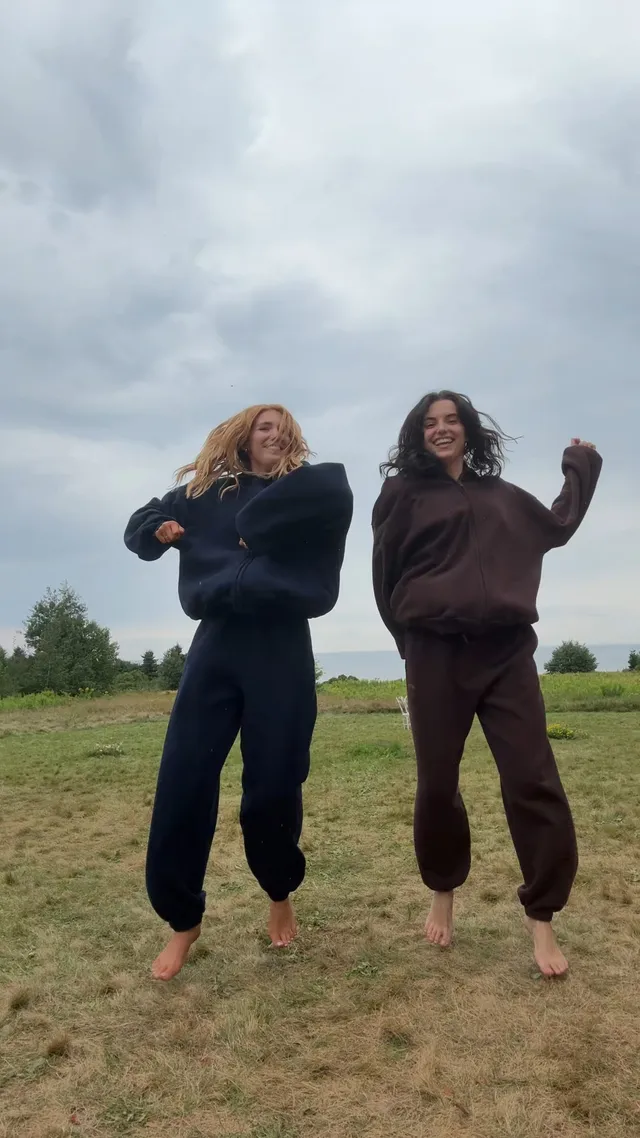 Sophie Nélisse jumping barefoot on grass beside another woman.