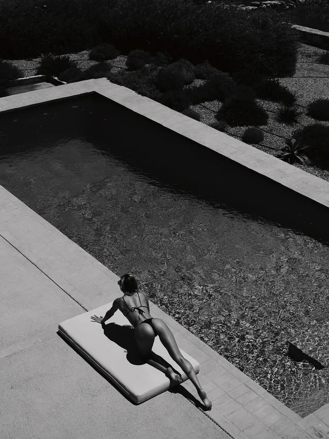 Candice Swanepoel reclining barefoot on a garden lounger in a monochrome photo.