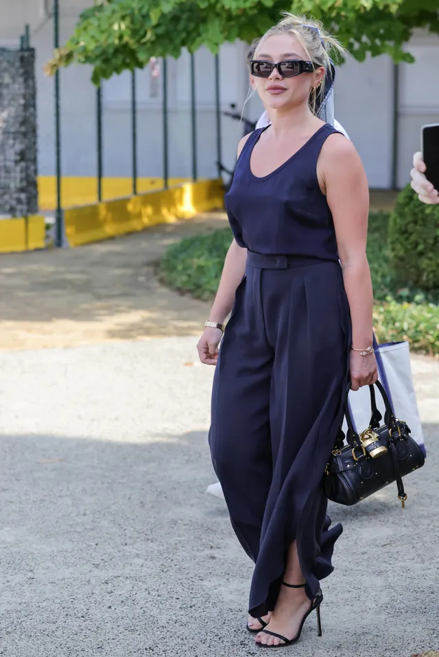 Florence Pugh walking outdoors in a navy outfit and black heels.
