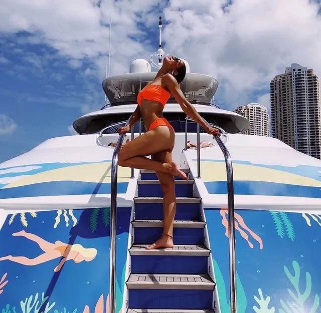 Samantha Logan posing barefoot in an orange bikini on a boat staircase.