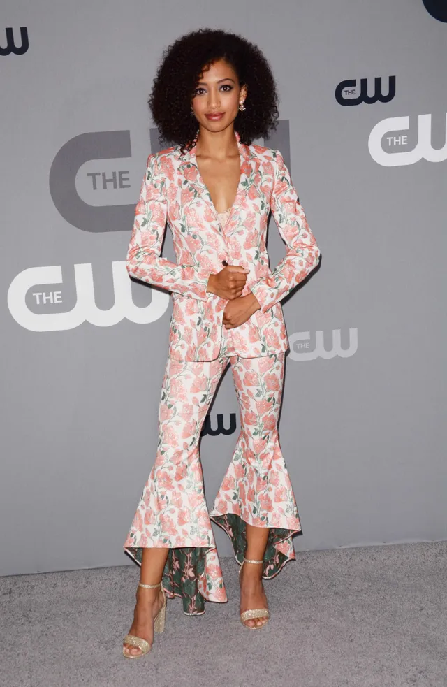 Samantha Logan wearing a floral trouser suit and gold heels before an event backdrop.