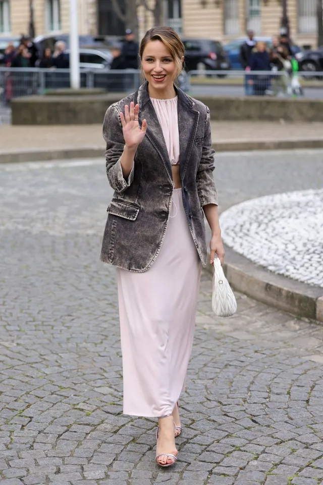 Dianna Agron walking on a cobbled path in a jacket and pale skirt.