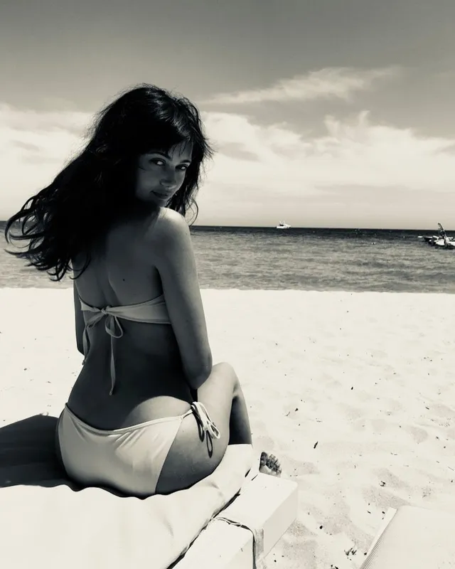 Ella Purnell sitting on a beach in a monochrome photograph.