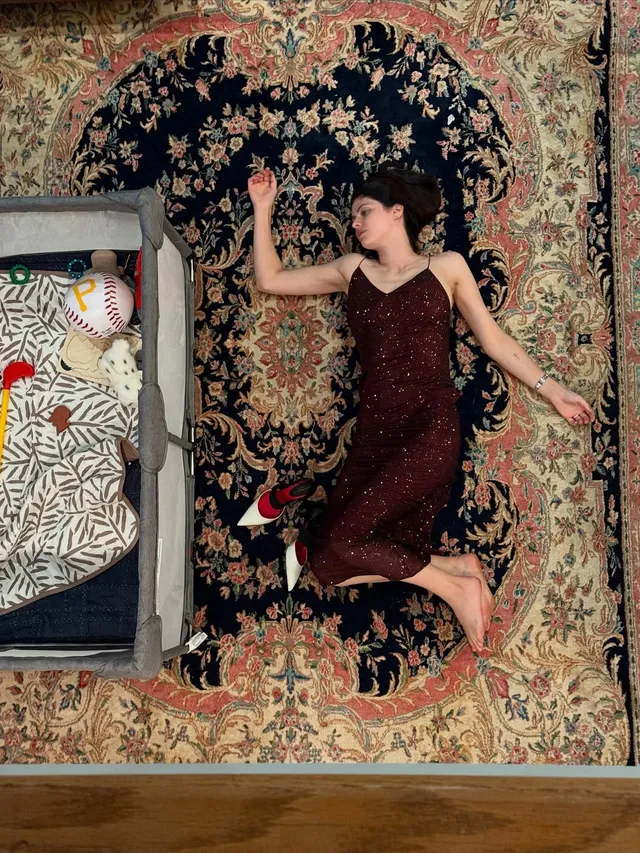 Alexandra Daddario lying barefoot on a patterned rug.