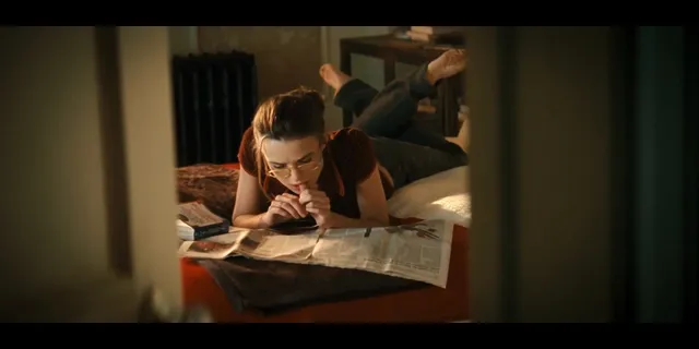 Keira Knightley a screen scene seated at a desk with feet raised behind her.