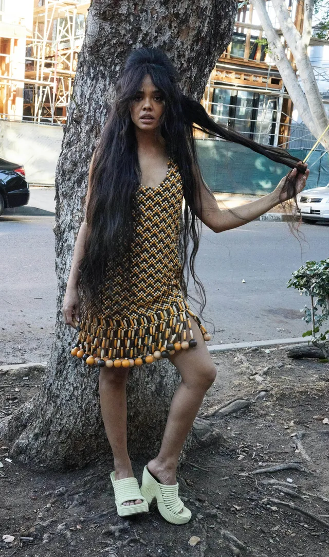 Tessa Thompson standing beside a tree in a patterned dress and chunky boots.