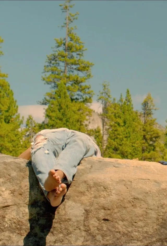 Zoë Kravitz reclining on a rock in jeans.