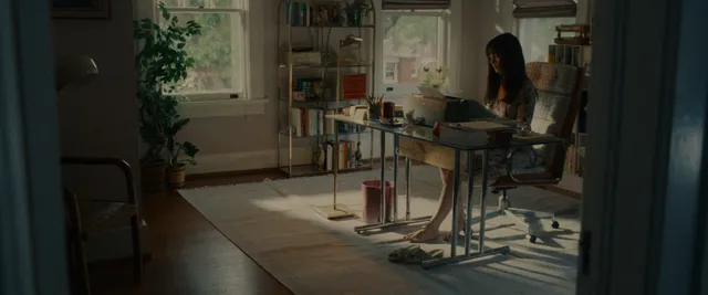 Anne Hathaway seated at a table in a softly lit screen scene.