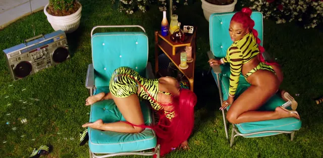 Nicki Minaj kneeling on an outdoor chair in a patterned outfit and bright heels.