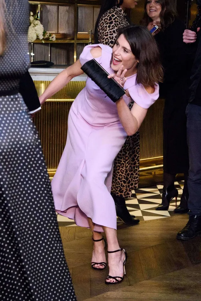 Gemma Arterton leaning toward a guest in a lavender dress.