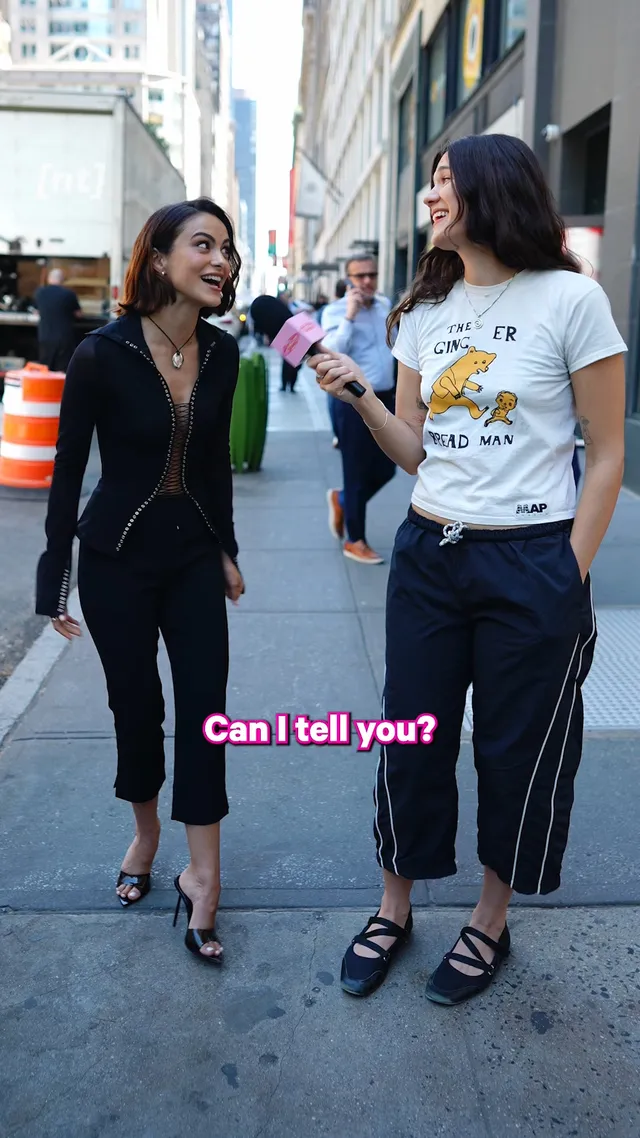 Camila Mendes standing with a friend during an outdoor interview in heels.