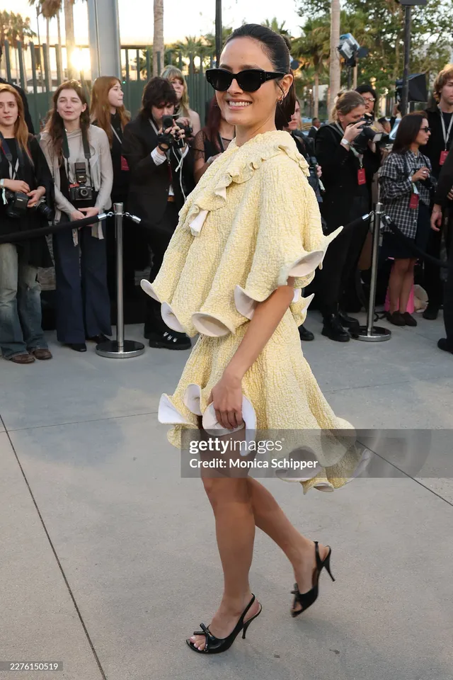 Chase Sui Wonders walking in a pale cape dress and black heels.