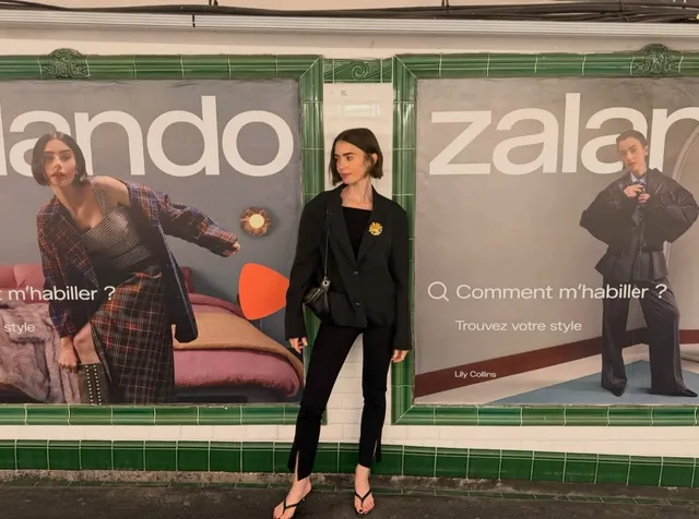Lily Collins posing outside in a dark suit and heels.