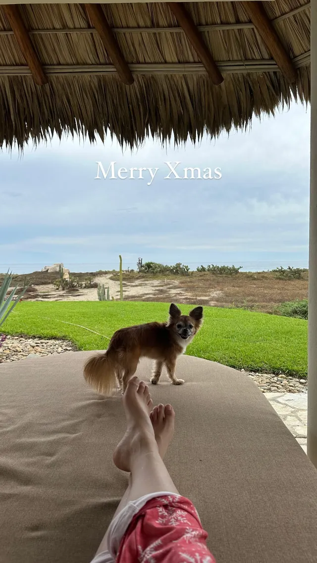 Melissa Barrera resting her bare feet on a lounger beneath a thatched roof.