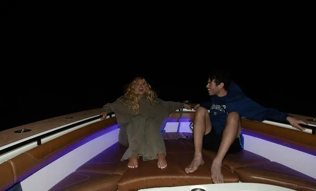 Iggy Azalea sitting barefoot on a boat beside another person at night.