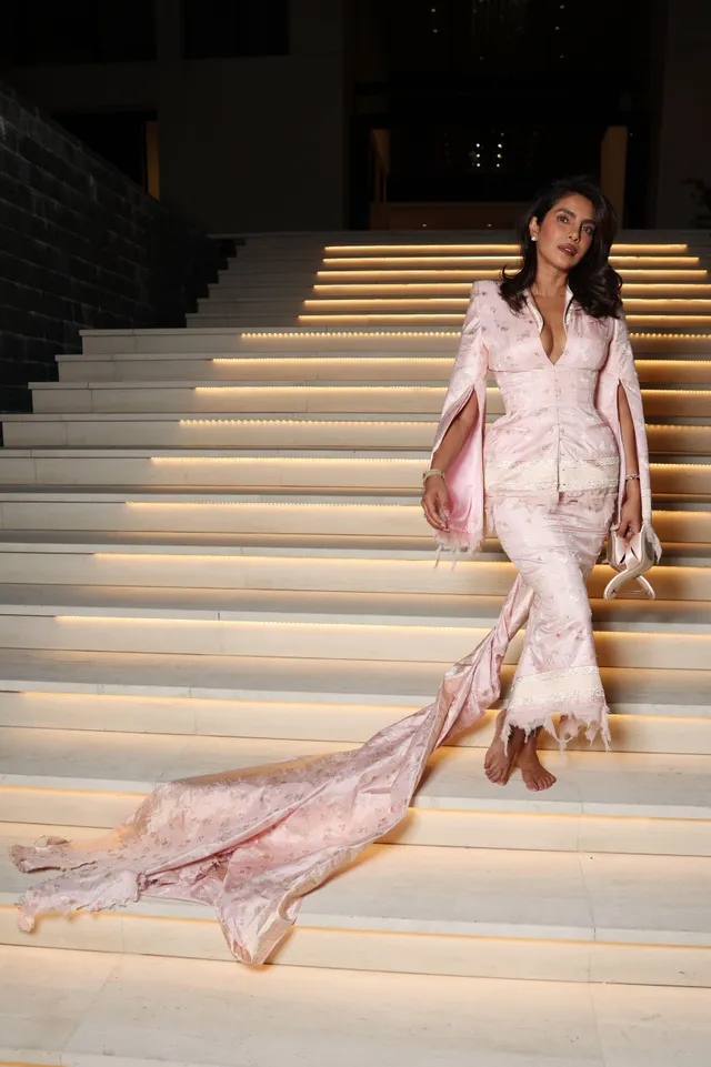 Priyanka Chopra Jonas walking down steps in pale heels and a long pink outfit.
