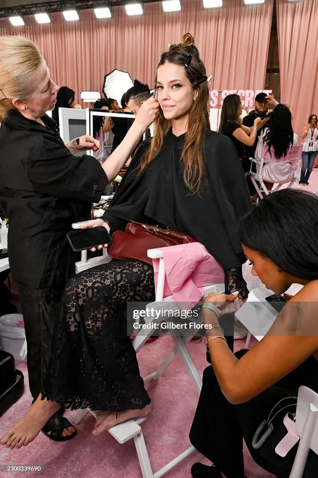 Barbara Palvin seated backstage with a bare foot extended during preparation.