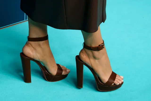 Blake Lively wearing dark ankle-strap heels on a carpet.