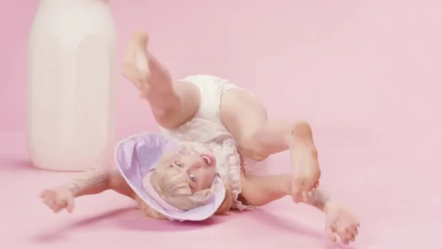 Miley Cyrus posing barefoot against a pink studio background.
