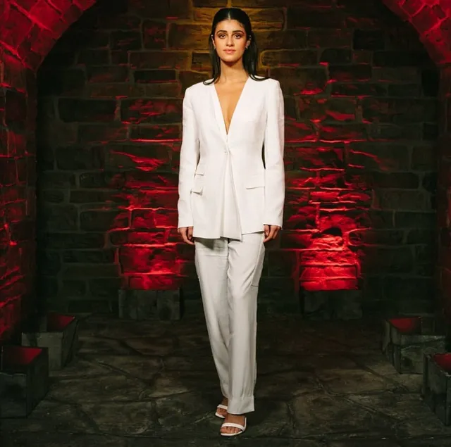 Anya Chalotra posing in a white trouser suit and pale heels.