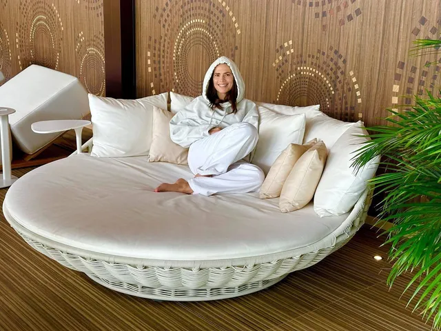 Hayley Atwell sitting on a round daybed in a white robe.