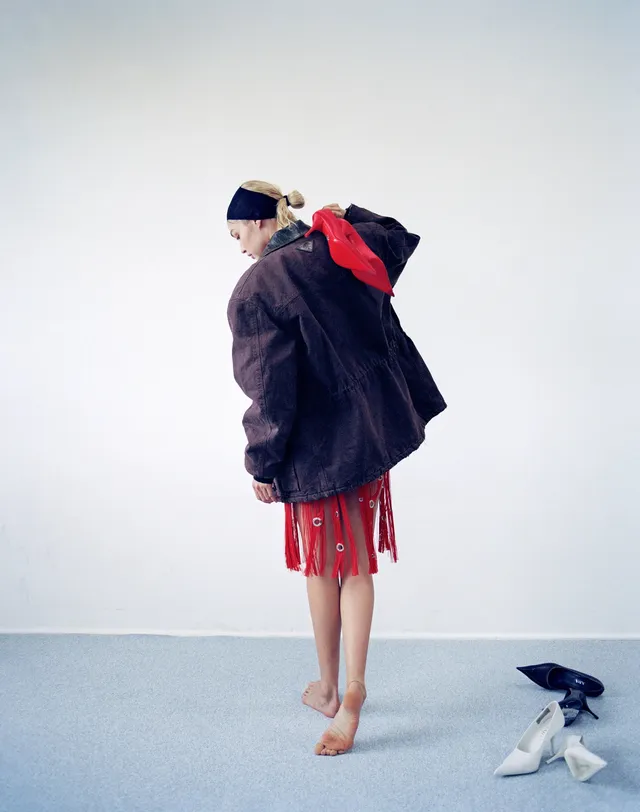 Gigi Hadid standing barefoot in a layered outfit for a studio portrait.