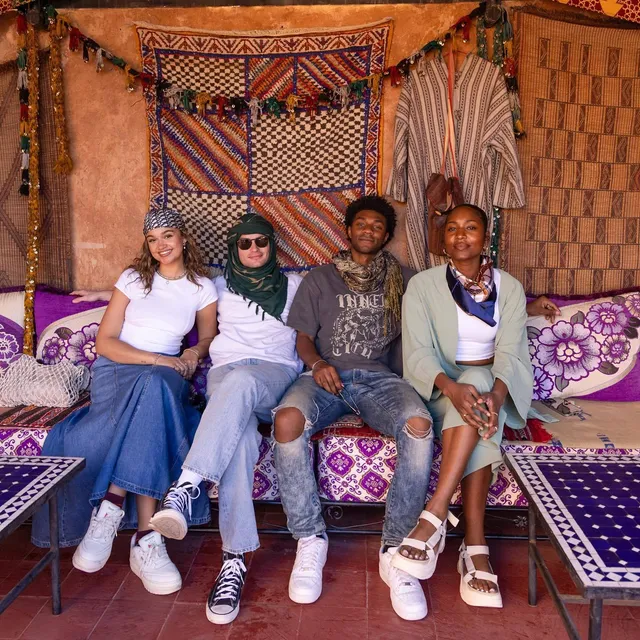 Carlacia Grant sitting with friends in a blue outfit and white flat sandals.