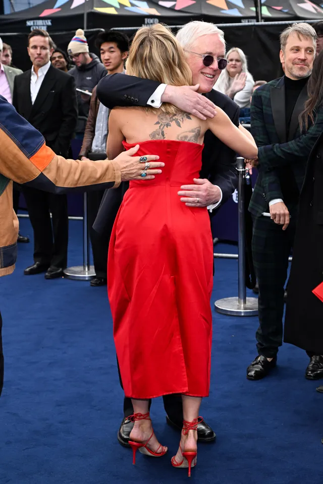 Scarlett Johansson greeting another person in a red dress and heels at a premiere.