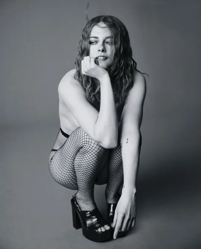 Kristen Stewart crouching in patterned stockings and platform heels in a monochrome portrait.