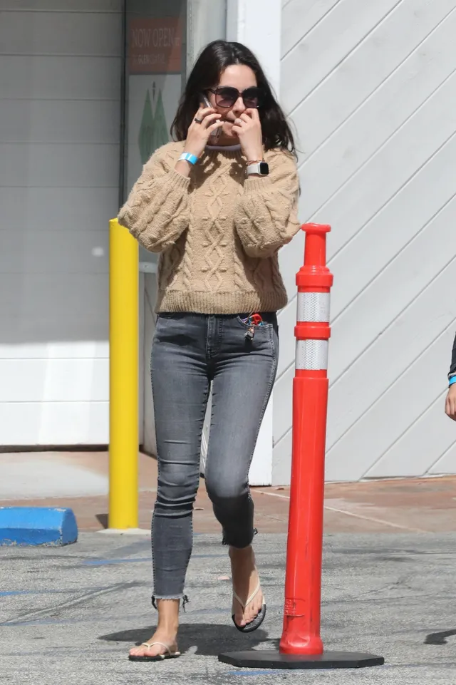 Mila Kunis walking in gray jeans and flip-flops.