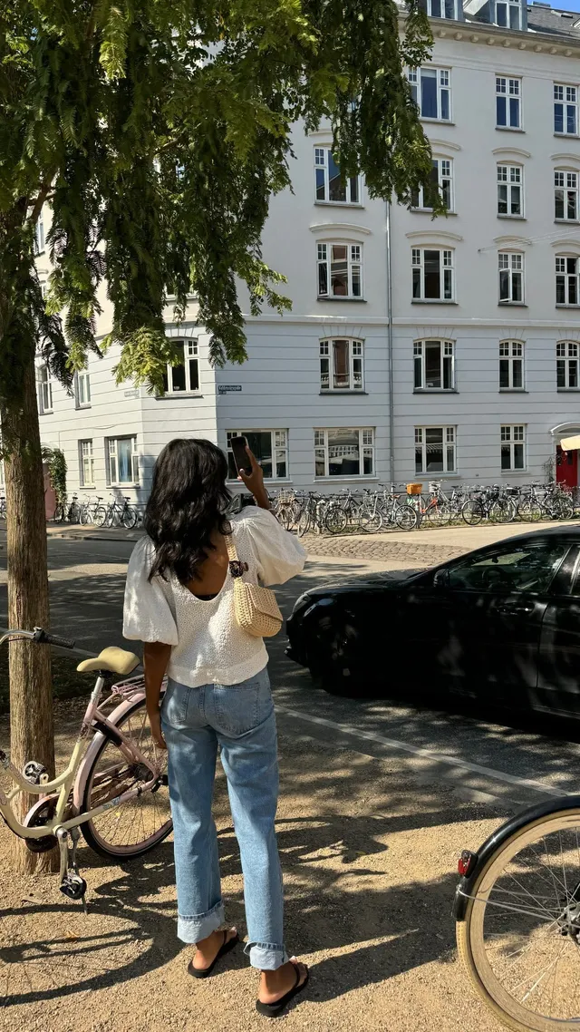 Greta Onieogou posing outdoors beside bicycles in jeans and flat shoes.