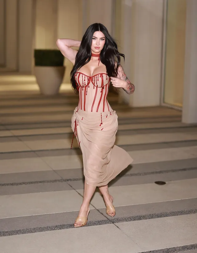 Megan Fox walking on a pavement in a pale dress.