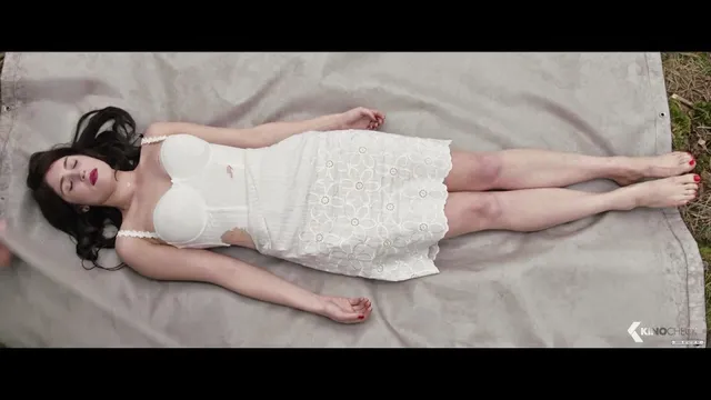 Gemma Arterton lying on a bed in a white dress in a screen scene.