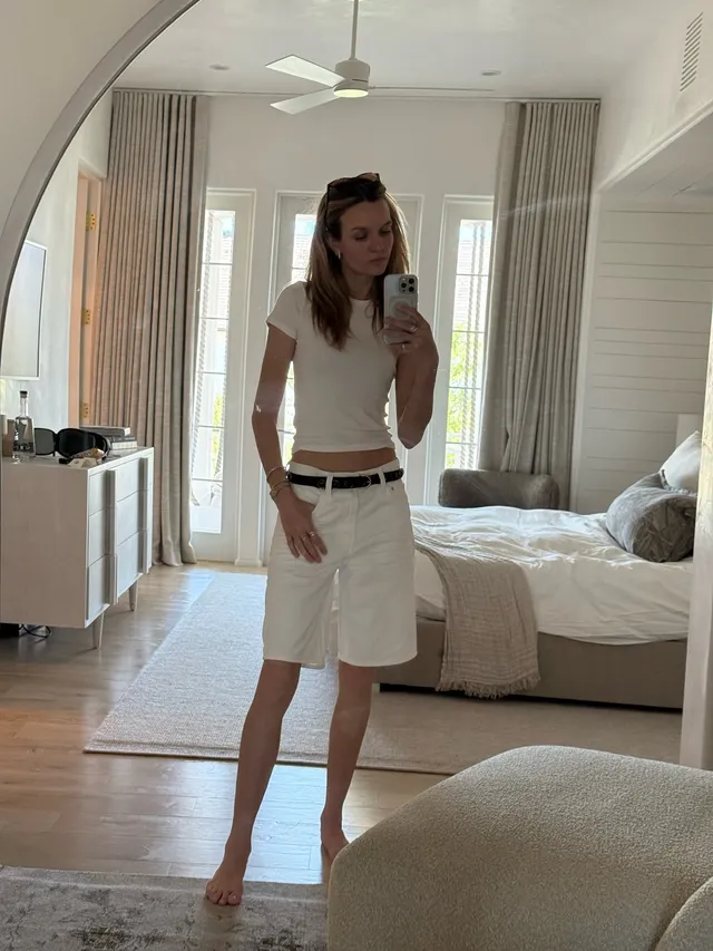 Josephine Skriver taking a barefoot mirror photograph in a white sleeveless outfit.