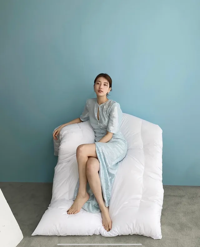 Bae Suzy sitting barefoot in a blue dress on a white chair.