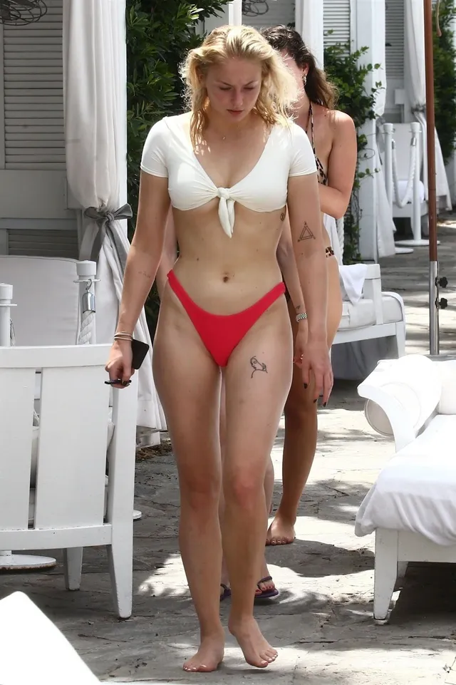 Sophie Turner a white tied shirt and red swimwear poolside.