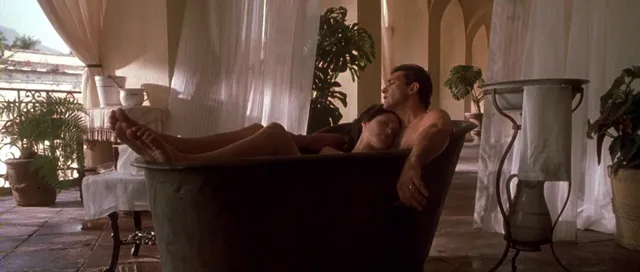 Angelina Jolie a reclining screen scene in a room with tall curtains.