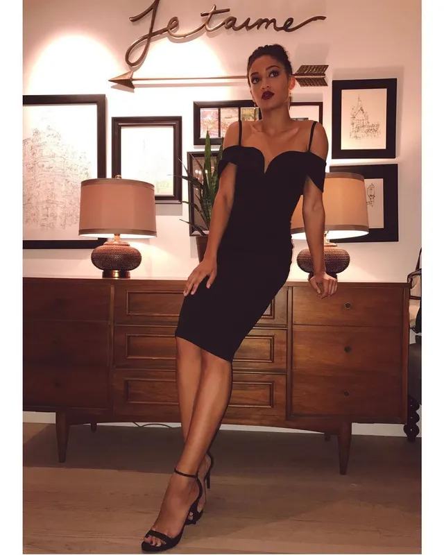 Samantha Logan posing indoors in a black dress and strappy heels.