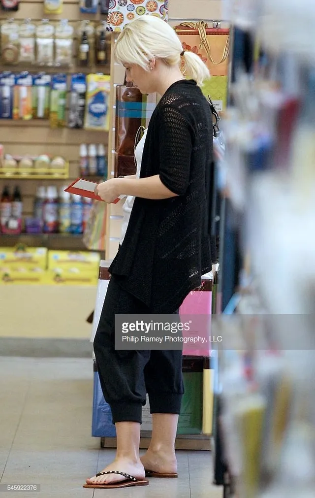 Elisha Cuthbert standing inside a shop in cropped trousers and flip-flops.