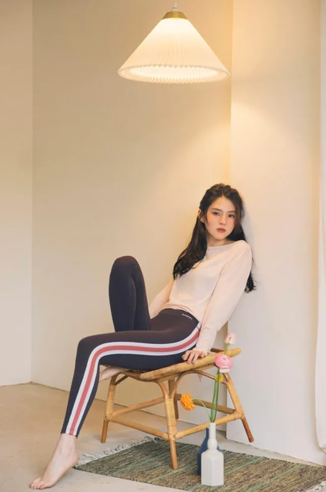 Han So-hee sitting barefoot in a white top and striped trousers.