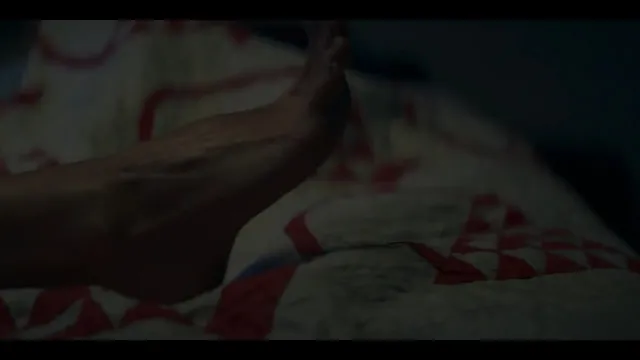 Alice Eve resting bare feet on patterned bedding in a scene.