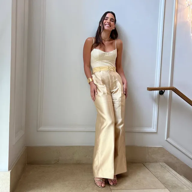 Adria Arjona wearing a cream outfit and open-toe heels on stairs.