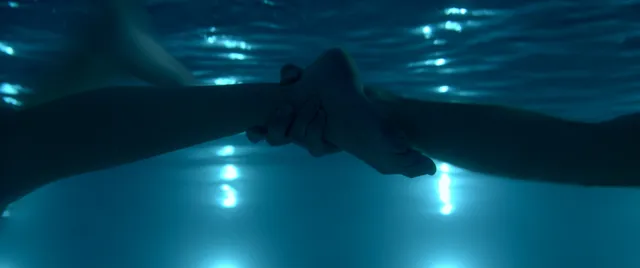 Maika Monroe swimming underwater in a blue-lit scene.