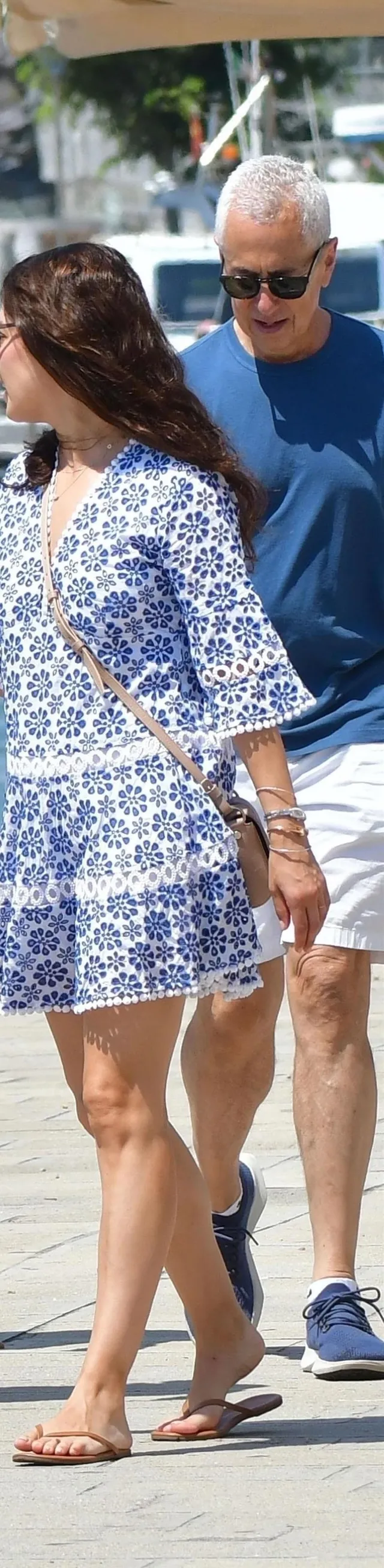 Mila Kunis walking in a patterned dress and flip-flops.