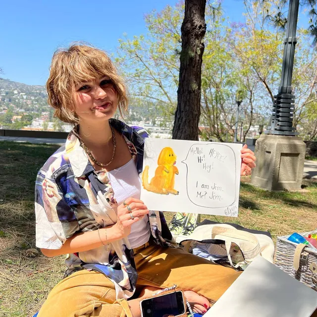 Debby Ryan sitting outdoors with a painting.